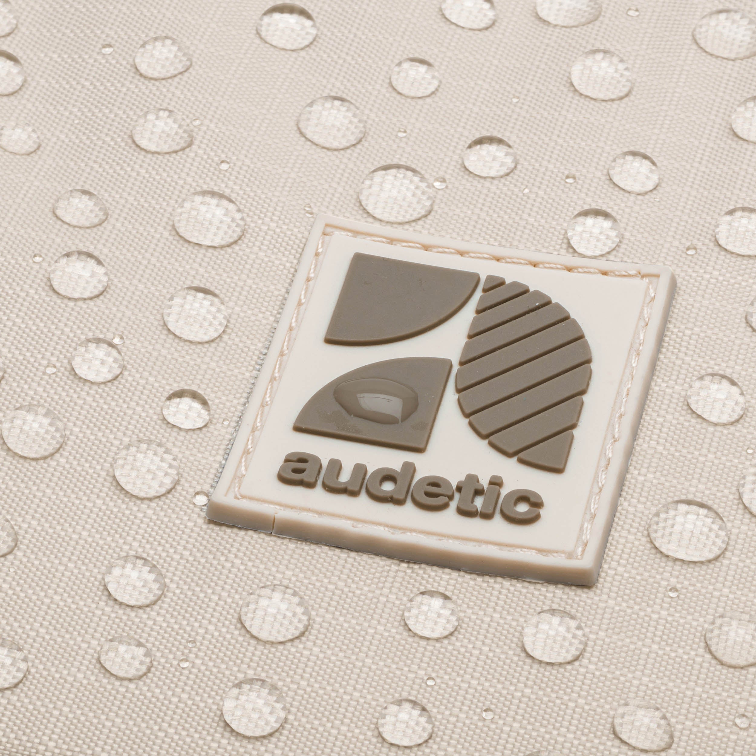 Nahaufnahme der wasserabweisenden Oberfläche und des beige-grauen audetic Logos auf der Bauchtasche DRIP