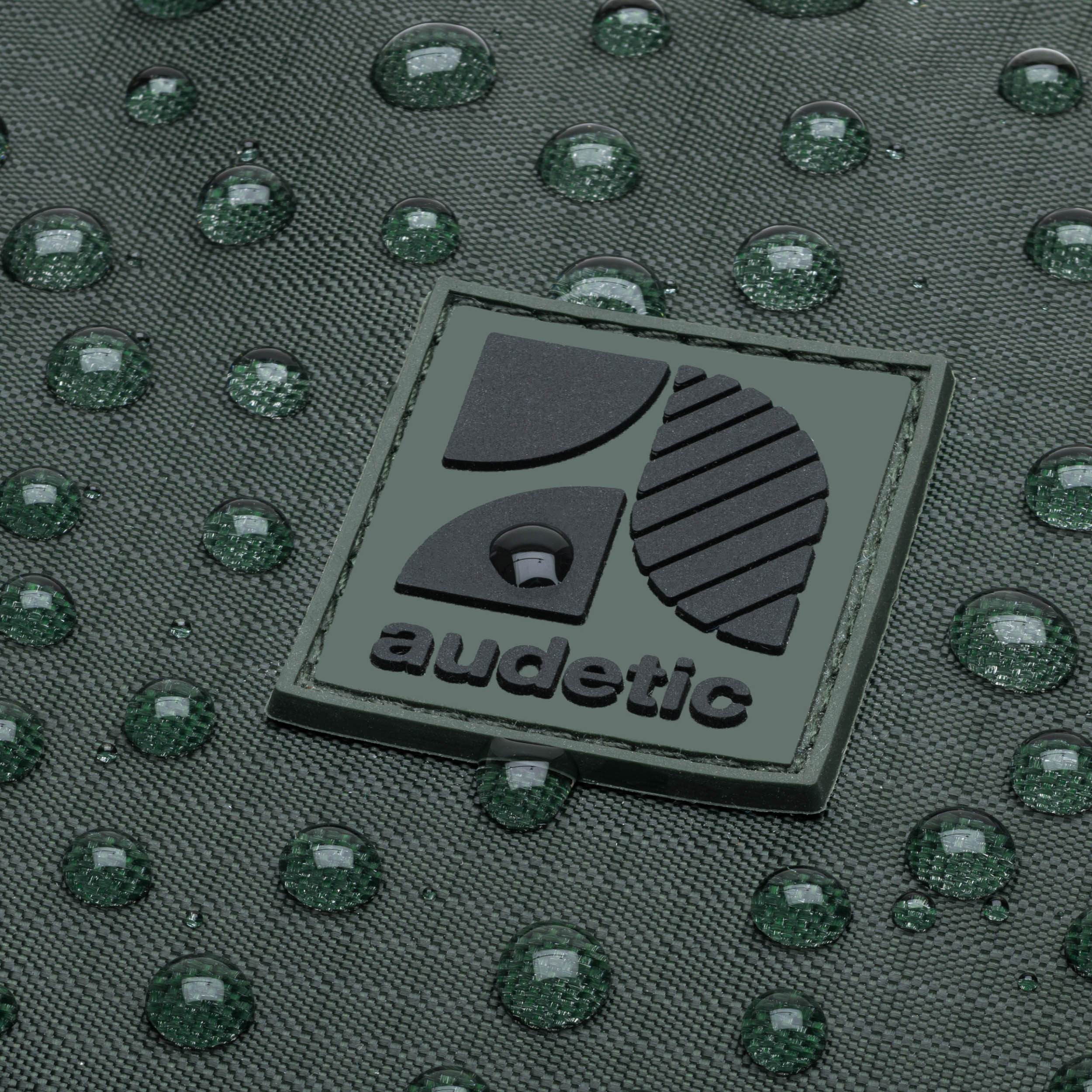 Nahaufnahme des dunkelgrünen, wasserabweisenden Materials der Bauchtasche DRIP mit audetic Logo