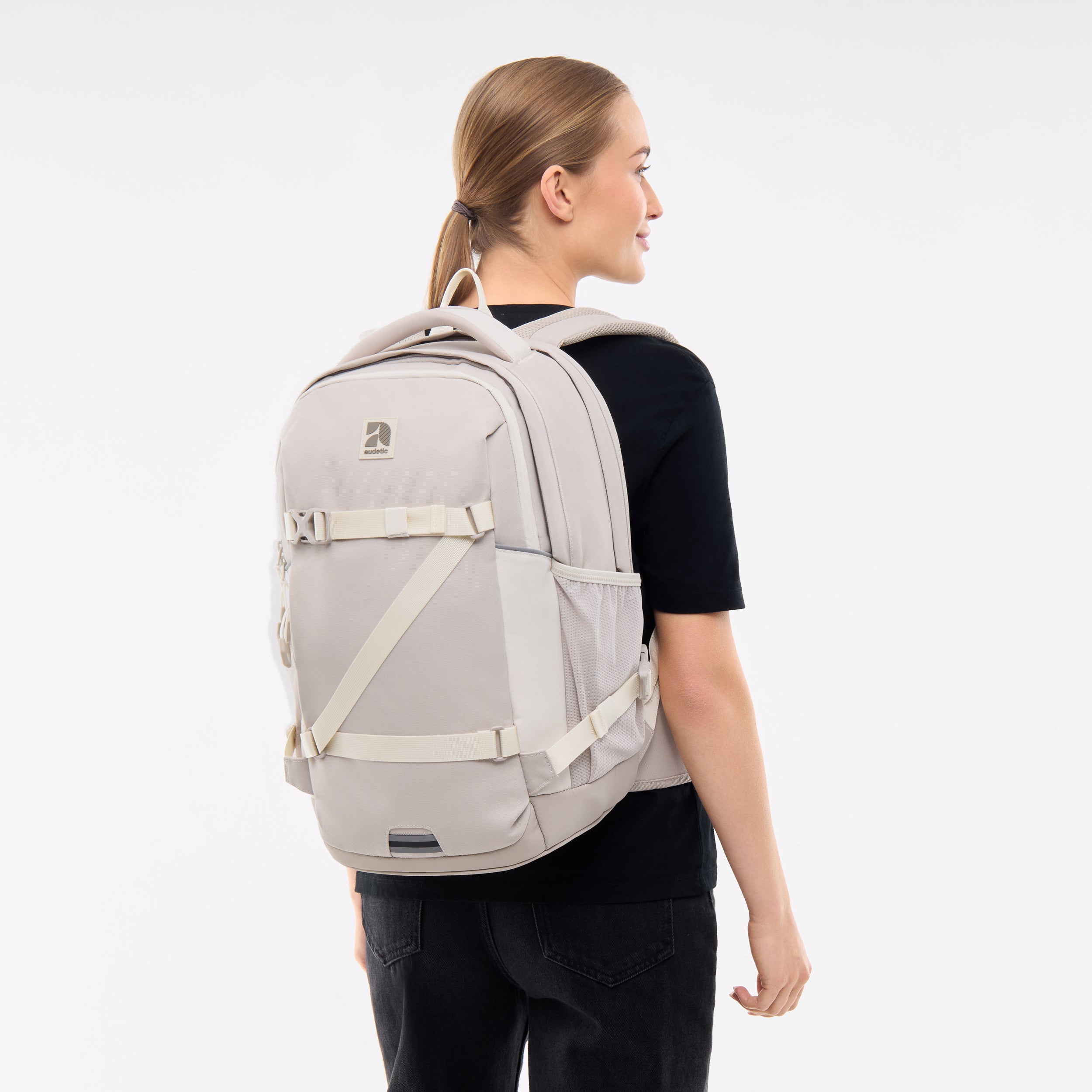 Junge Frau mit seitlich gebundenem Pferdeschwanz trägt sandfarbenen schulrucksack COSMO von Audetic auf dem Rücken