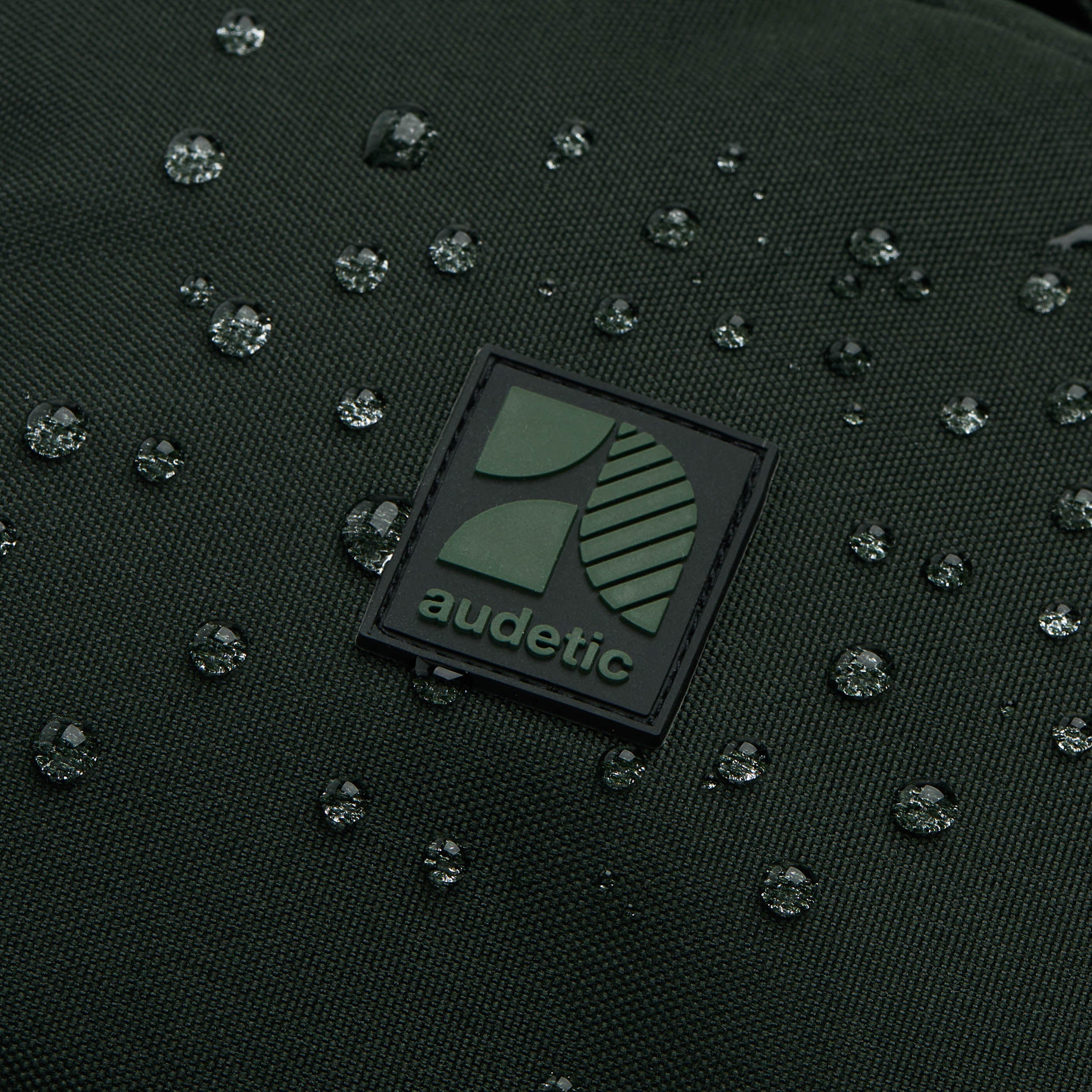 Nahaufnahme des wasserabweisenden Materials des Schulrucksacks FLEX von Audetic mit Logo und Wassertropfen