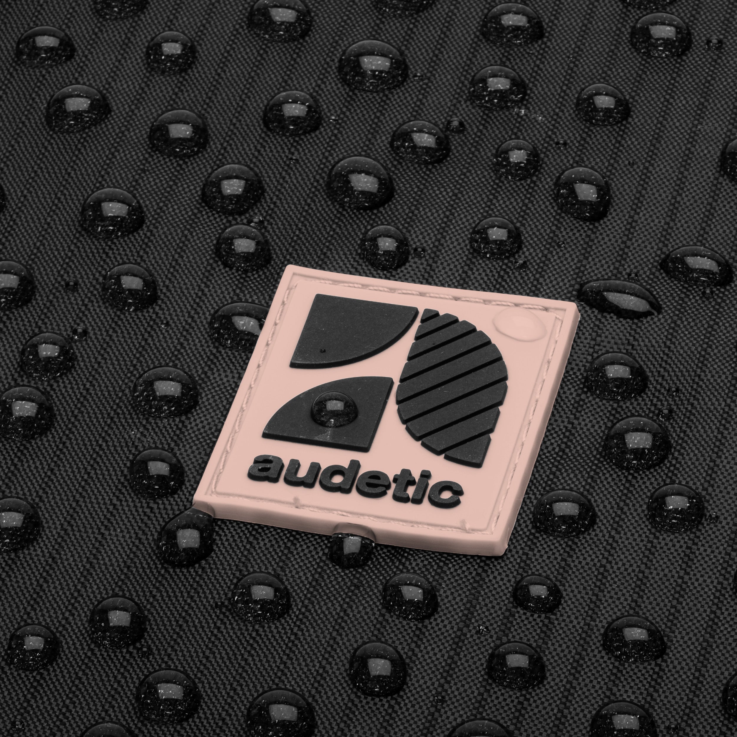 Nahaufnahme des wasserabweisenden schwarzen Stoffes eines Turnbeutels mit rosa Audetic-Logo und Wasserperlen