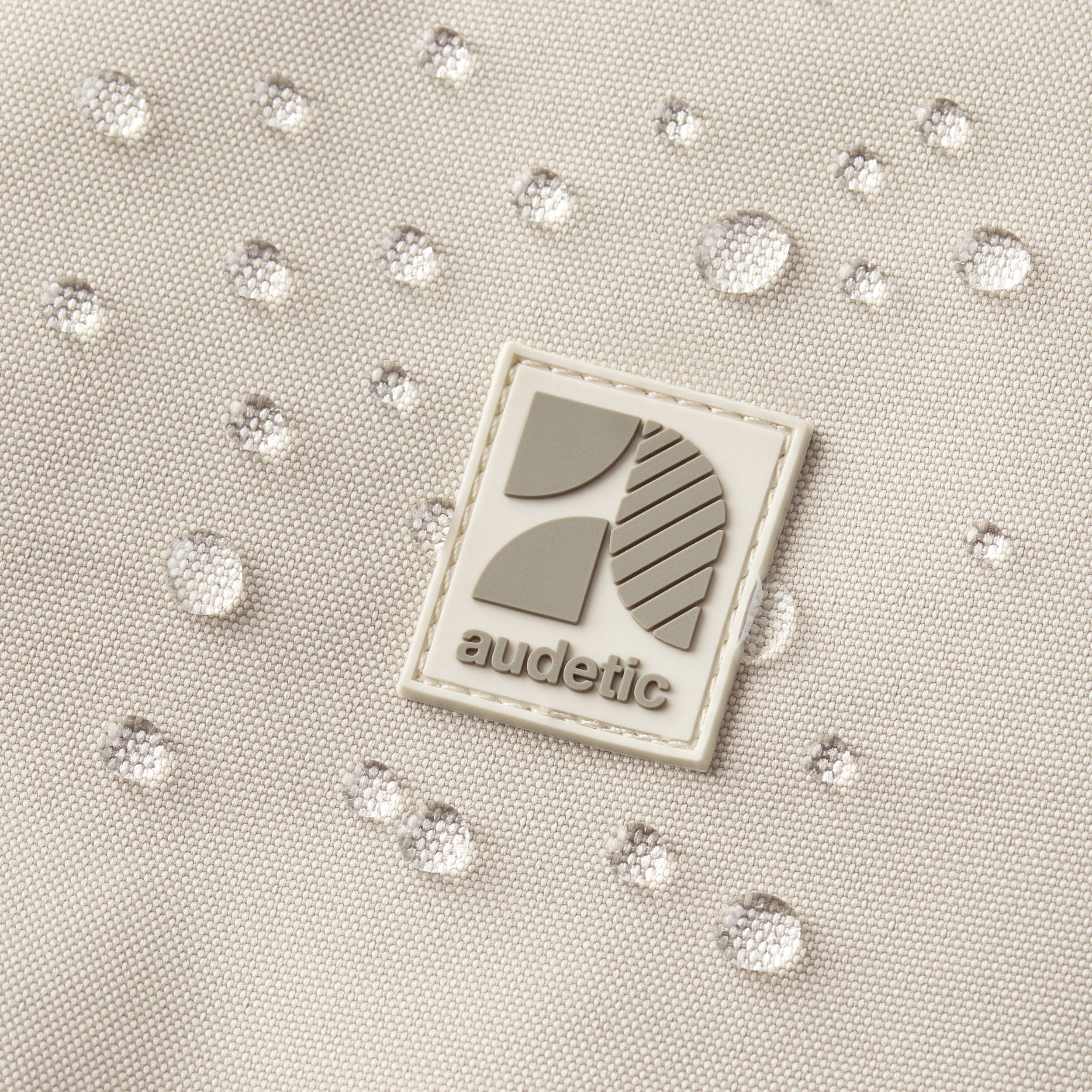Nahaufnahme des audetic-Logos auf wasserabweisendem Stoff mit Wassertropfen