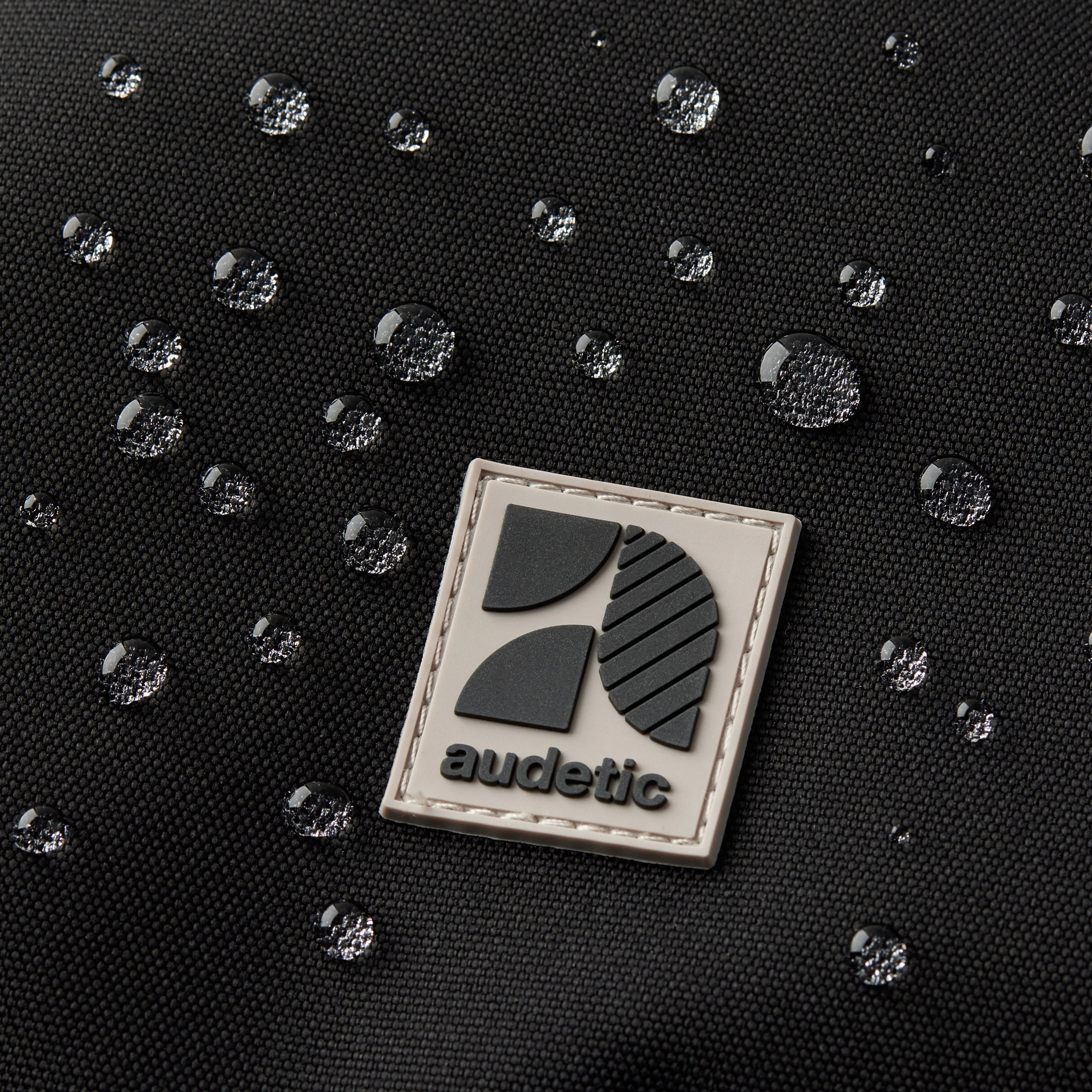 Nahaufnahme des wasserabweisenden Materials und Logos des schwarzen FLEX Schulrucksacks von audetic