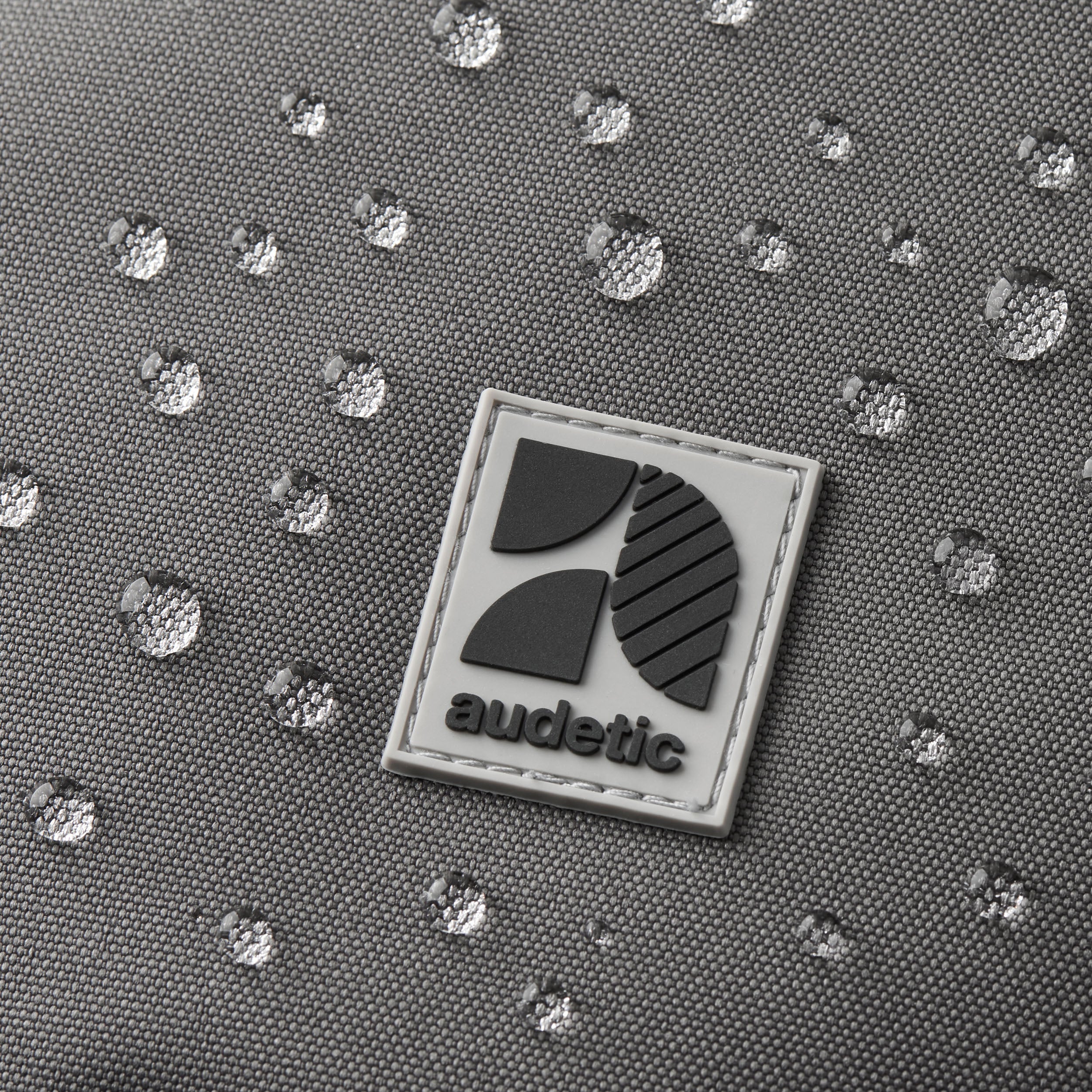 Wasserfeste graue Textiloberfläche mit abperlenden Wassertropfen und Audetic-Logo