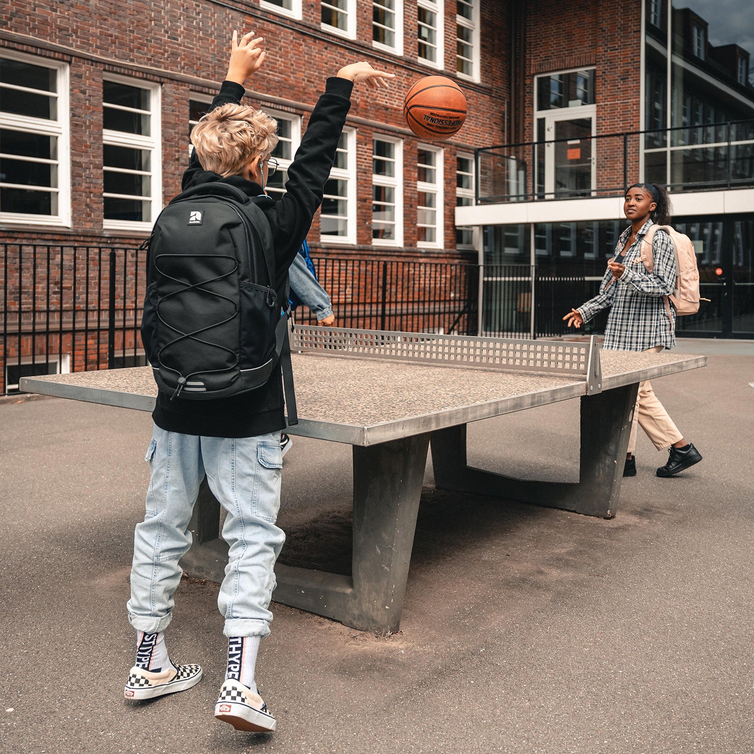 Teenager-Junge mit schwarzem Schulrucksack AERO spielt Basketball vor einer Tischtennisplatte
