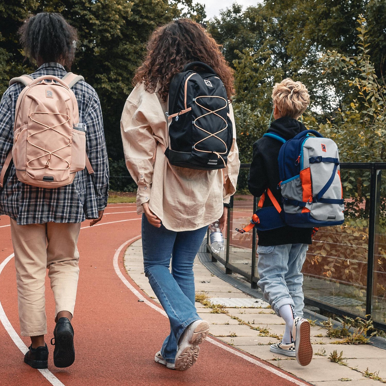 Drei Jugendliche gehen auf einer Laufbahn, zwei tragen den Schulrucksack AERO in schwarz-rosa